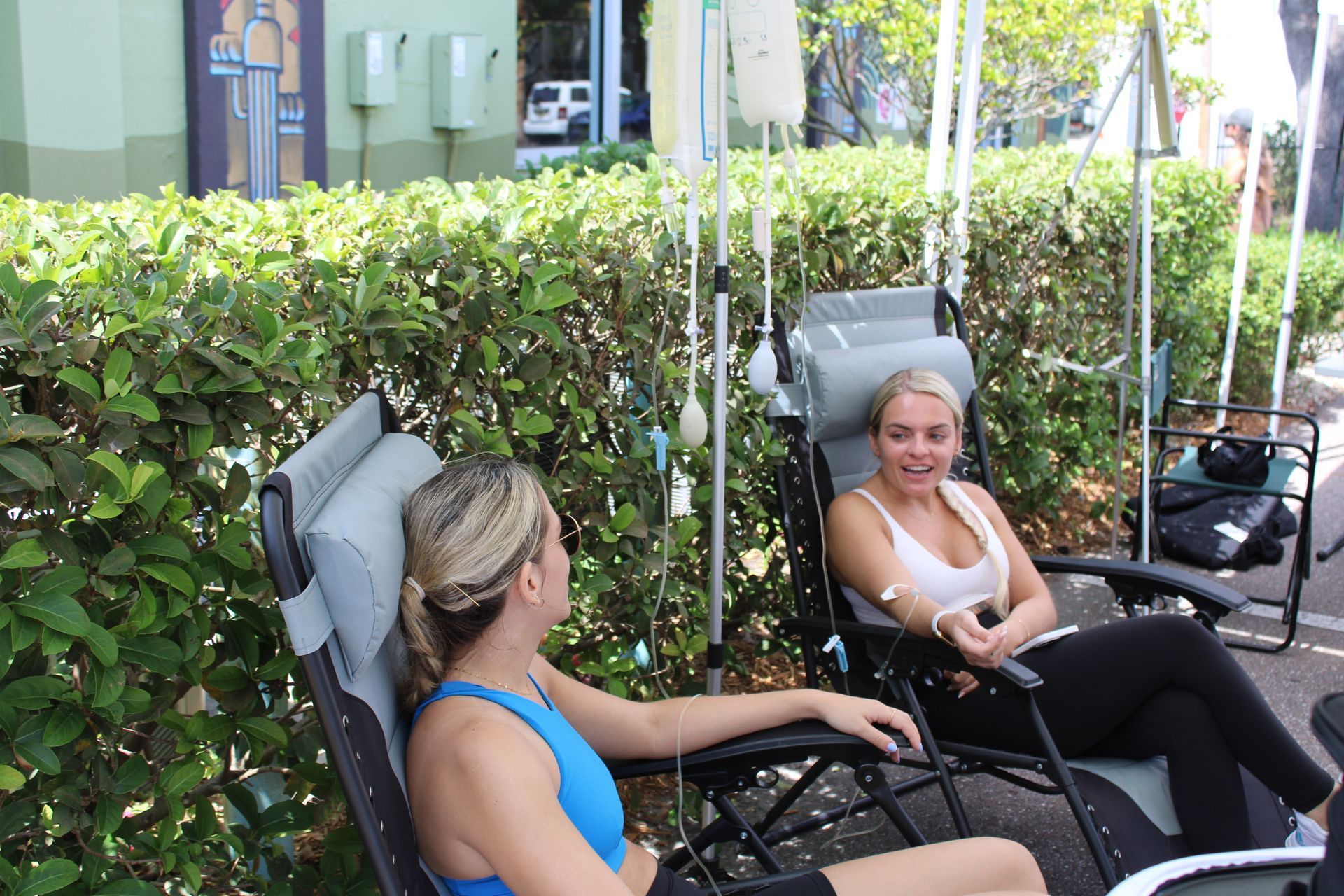 two women are sitting in chairs in front of a hedge .