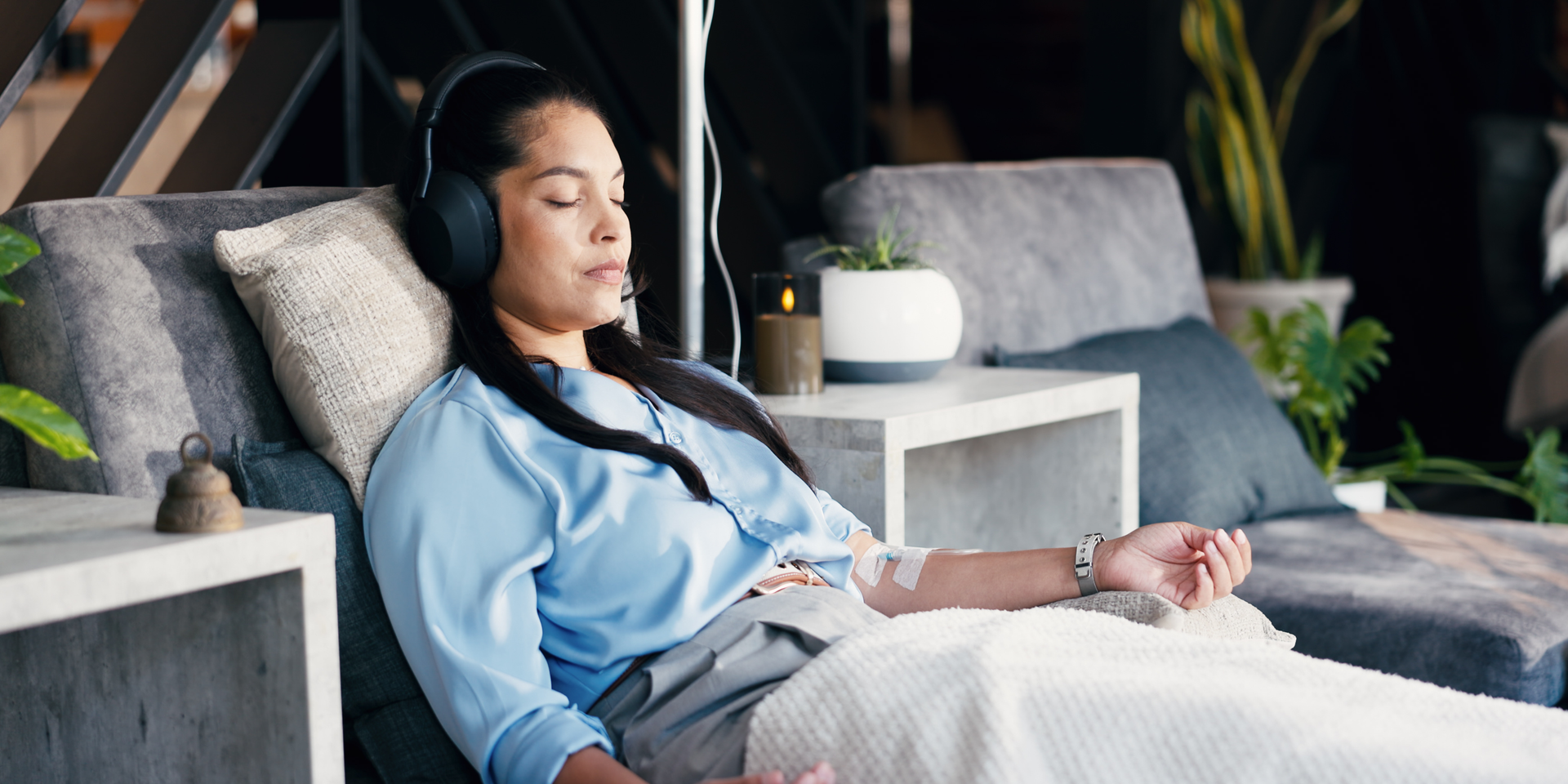 A person reclines on a lounge chair, eyes closed and wearing headphones, receiving intravenous therapy in a calm room.