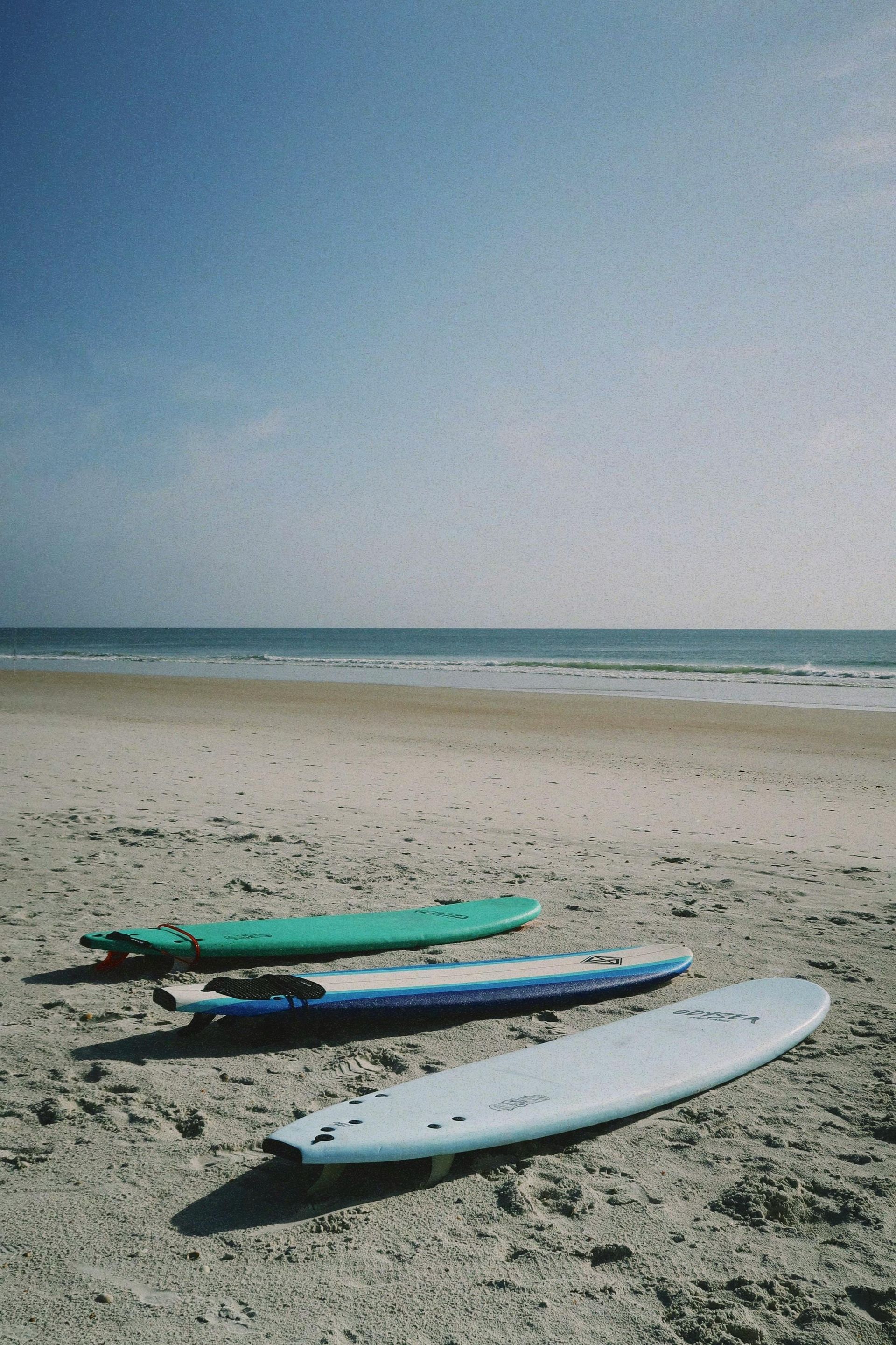 Three surfboards are sitting on a sandy beach near the ocean
