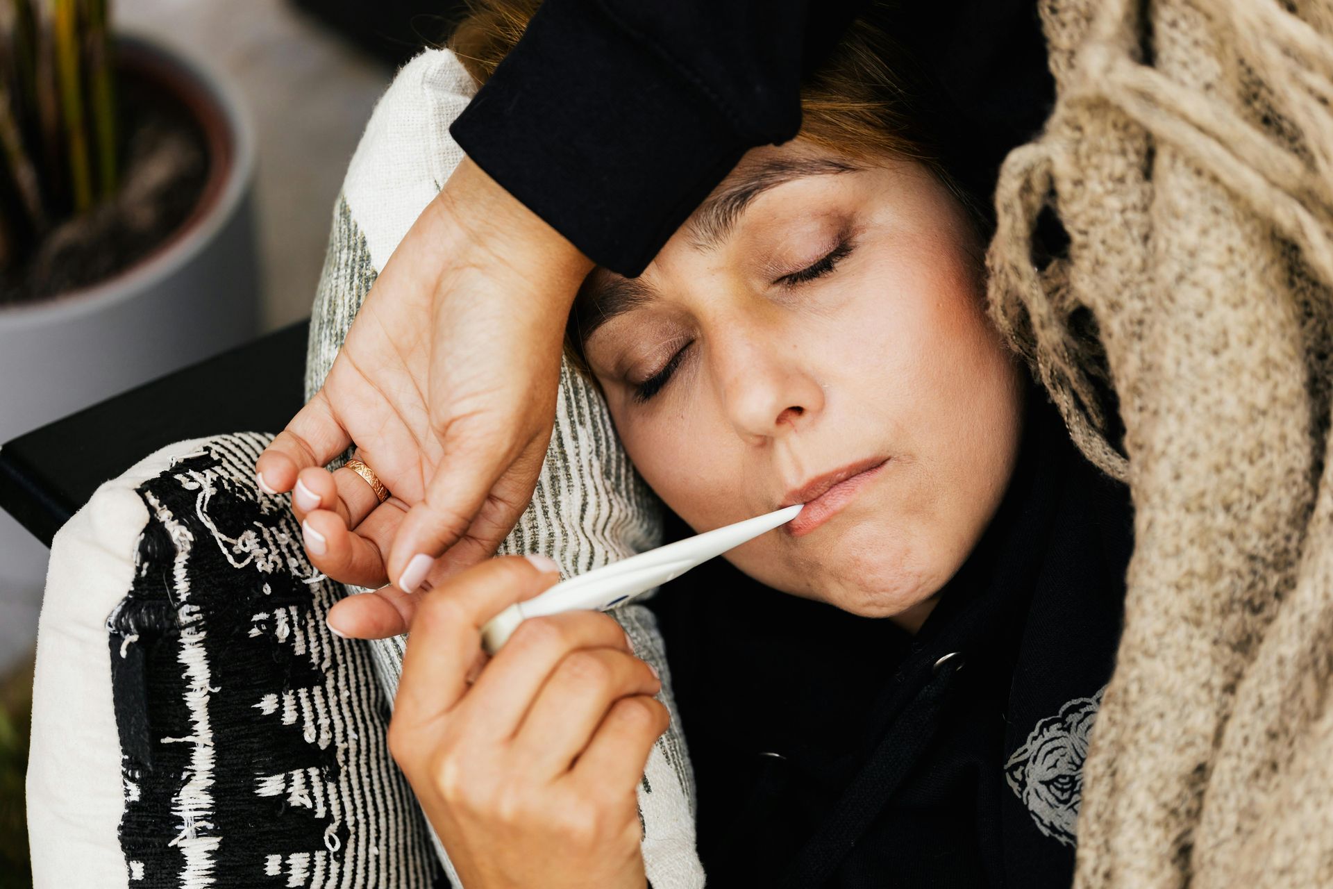 A woman in bed, taking her temperature, appears ill.