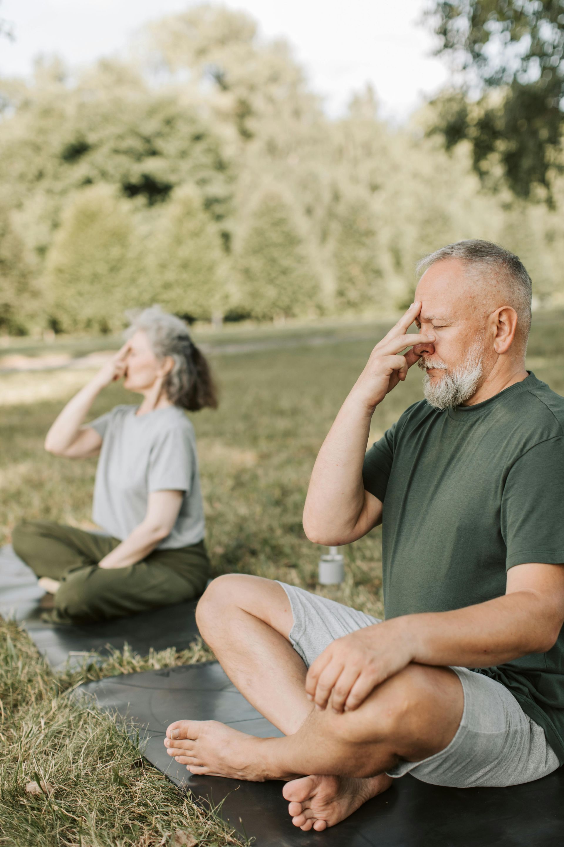 A man and a woman are sitting on a yoga mat in a park.