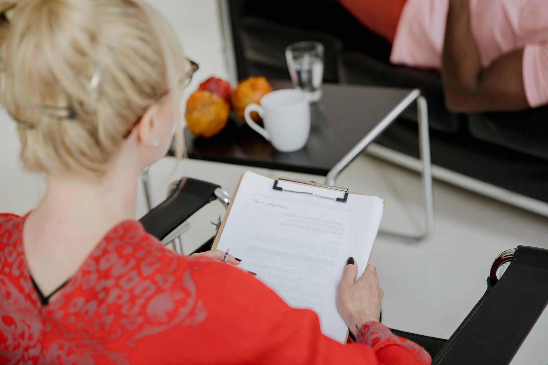 A woman is sitting in a chair holding a clipboard and writing on it.