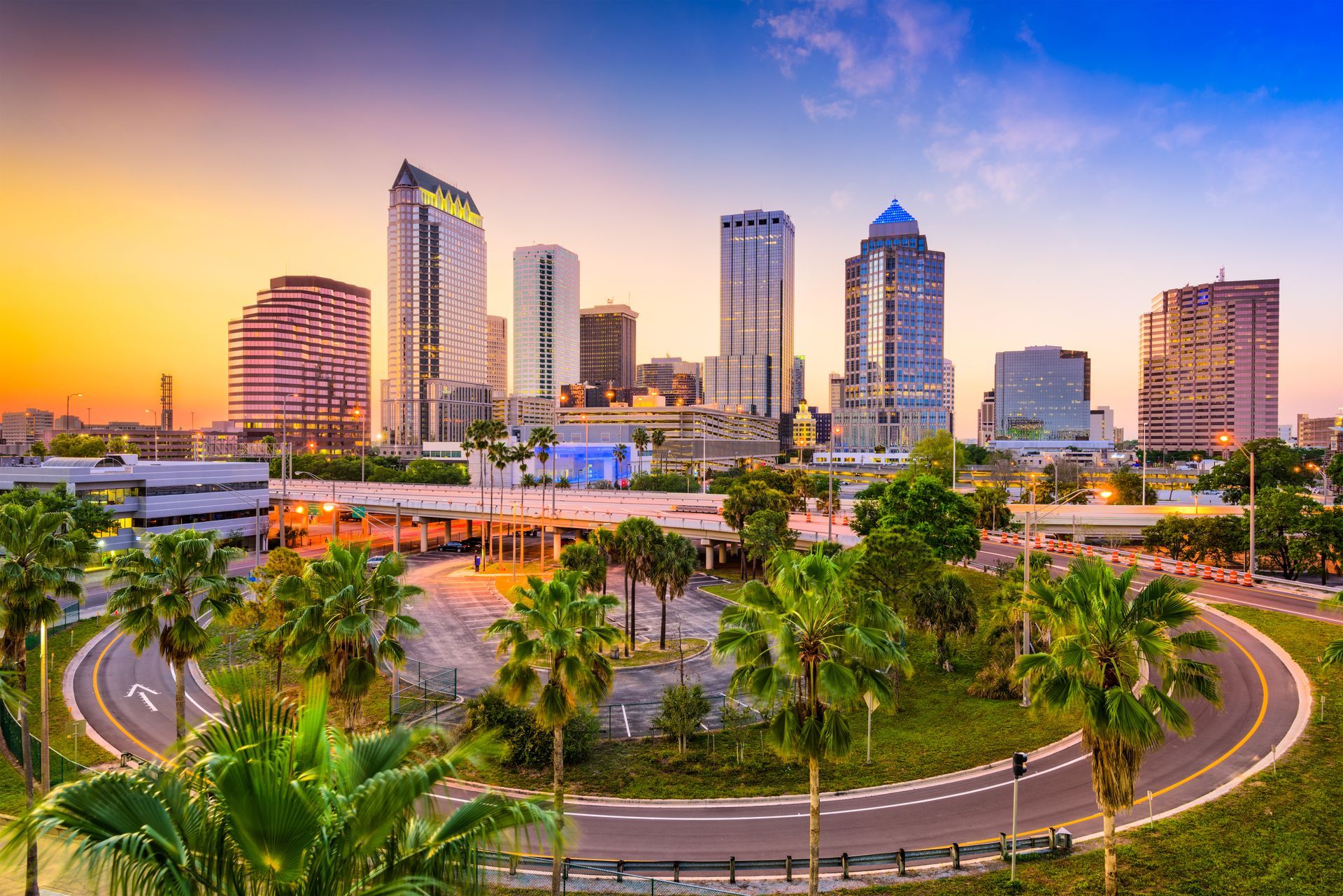 An aerial view of a the Tampa skyline at sunset with palm trees in the foreground.