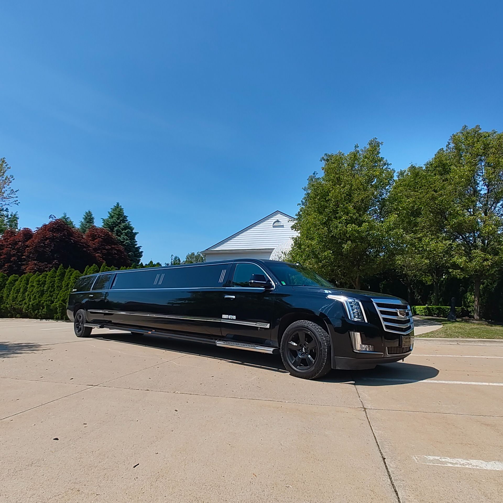 Black limousine parked in front of a white building under a blue sky, trees in the background.