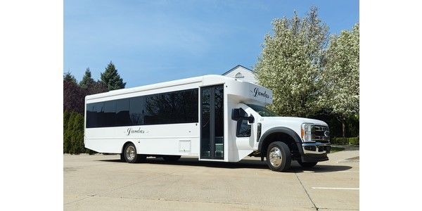 A white bus is parked in a parking lot with trees in the background.