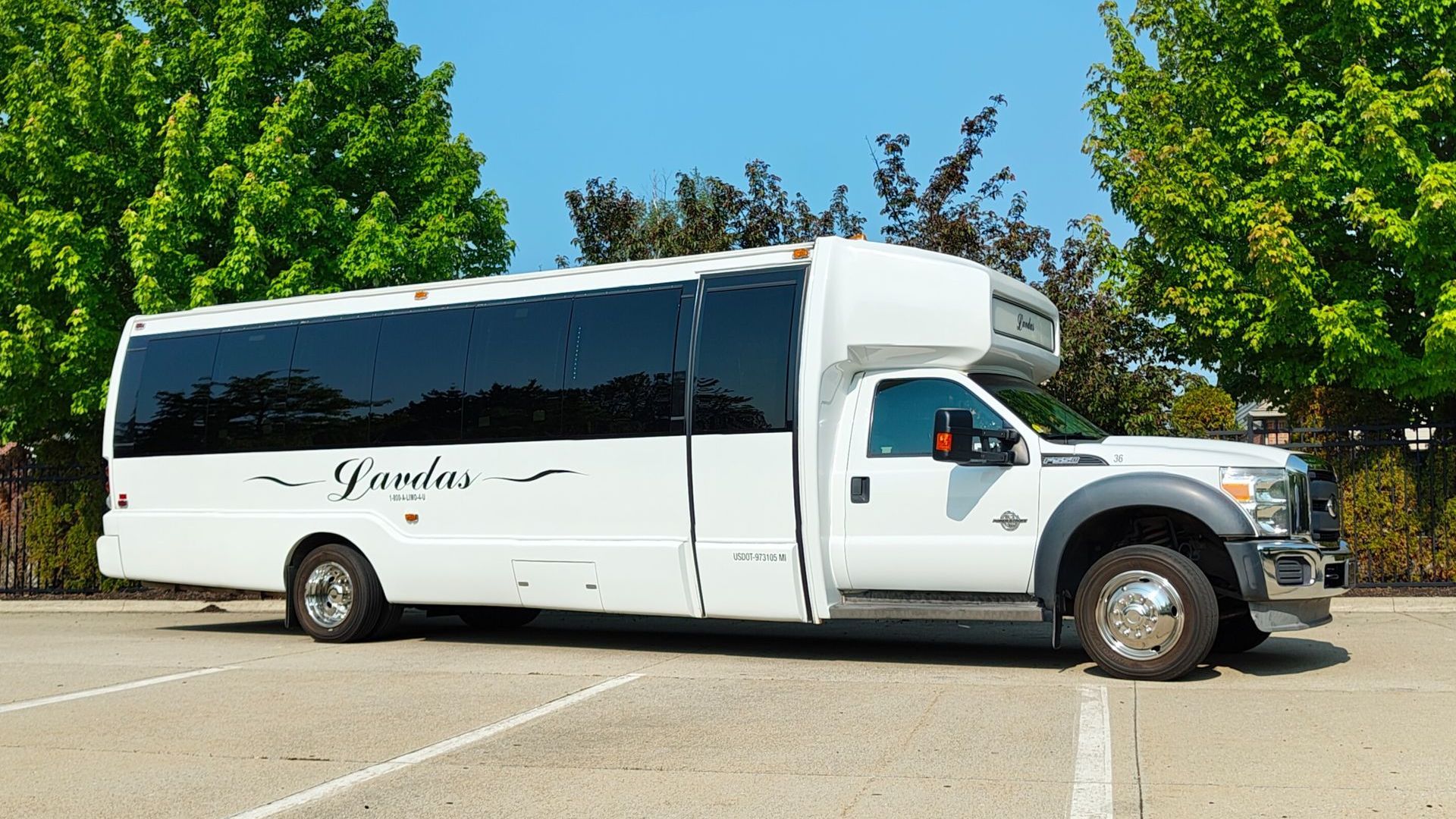 A white bus is parked on the side of the road in a parking lot.