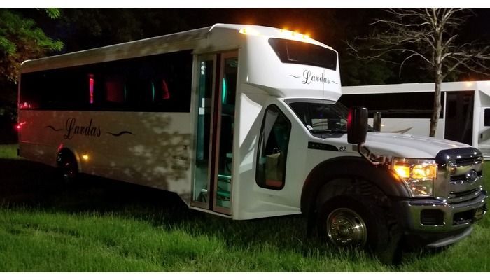 A white bus is parked in the grass next to a truck.