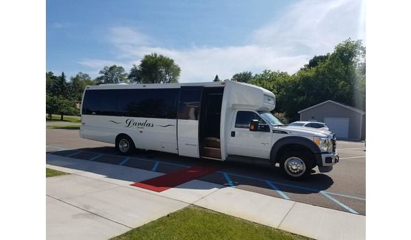 A white bus is parked on the side of the road in a parking lot.