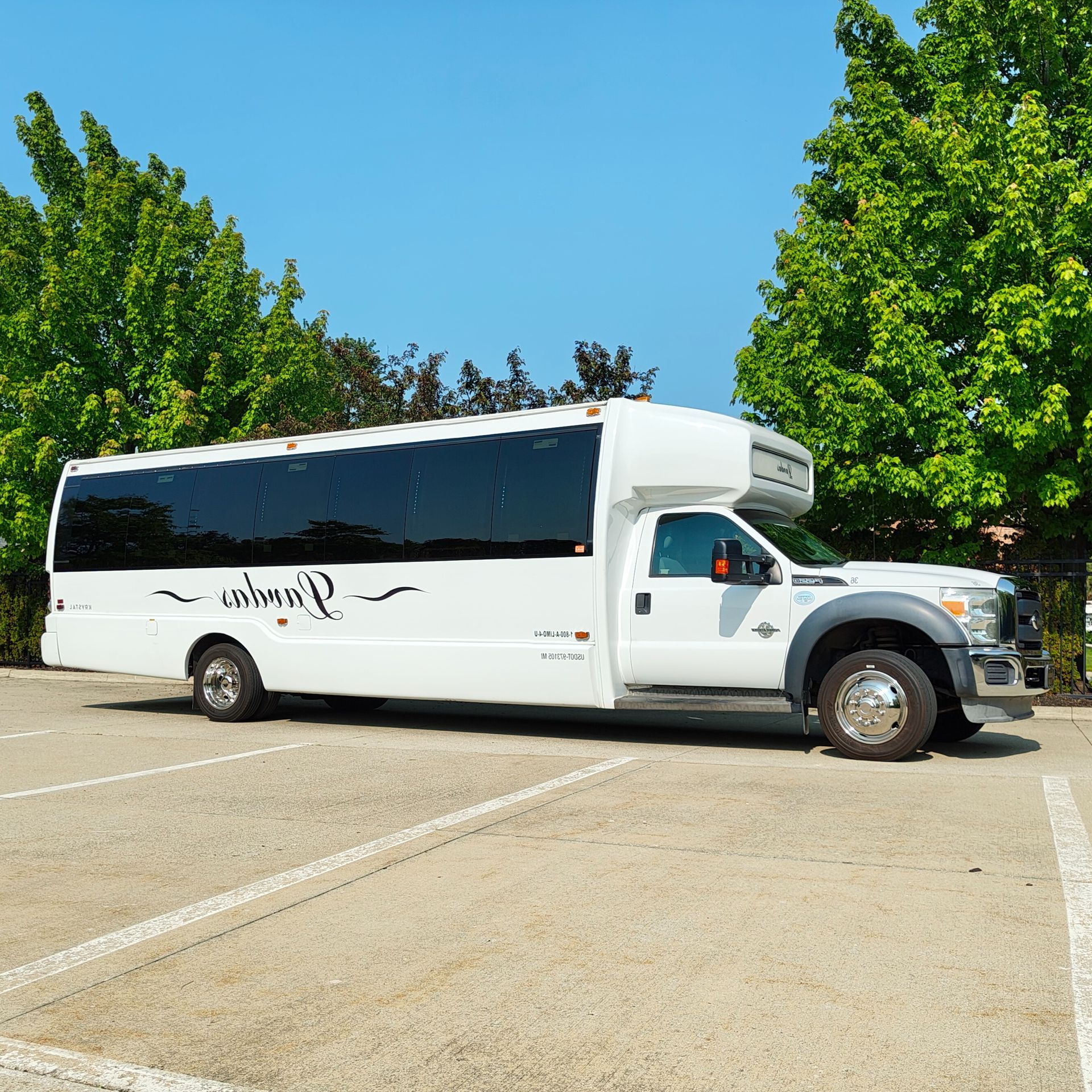 White party bus parked in a lot, with trees and blue sky visible.