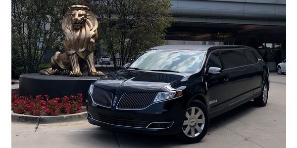 A black limousine is parked in front of a statue of a lion.