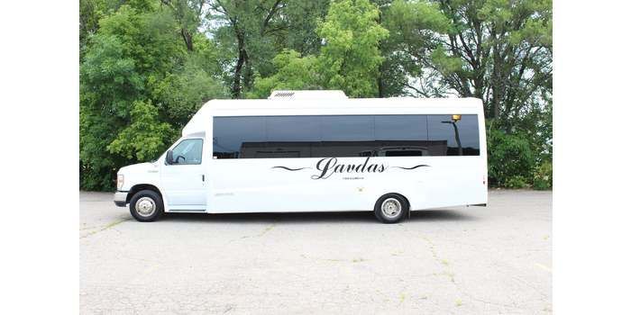 A white bus is parked in a parking lot with trees in the background.