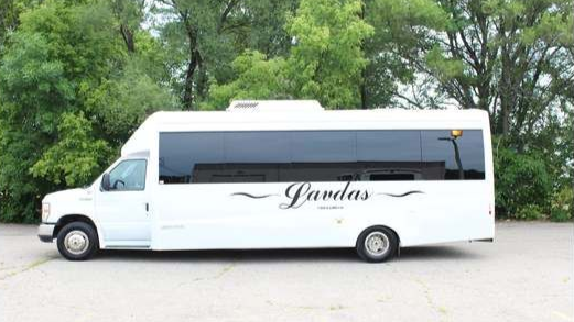 A white bus is parked in a parking lot with trees in the background.
