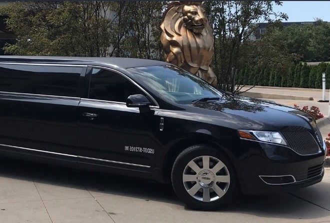 A black limousine is parked in front of a statue of a lion