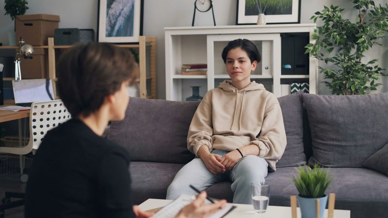 Therapist meeting with a seated client in a living-room office setting, with a coffee table in front.