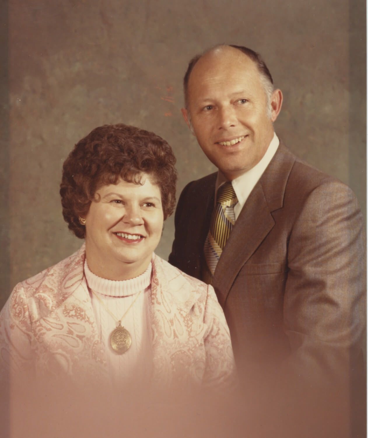 Couple smiling, woman in pink jacket, man in suit.