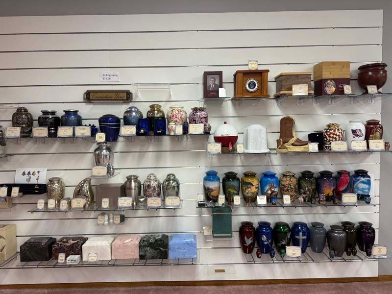 Display of cremation urns on shelves in a funeral home. Various shapes, sizes, and colors.