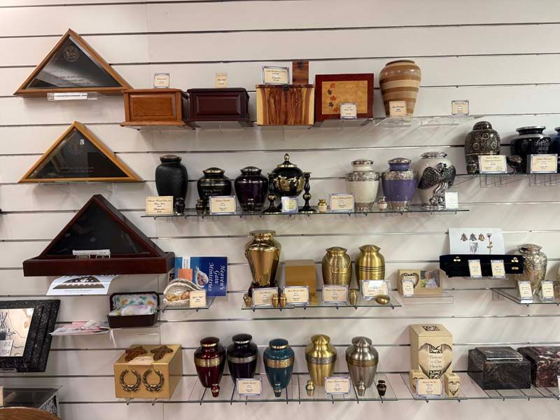 Shelves displaying various urns and display boxes for ashes, in a store setting.