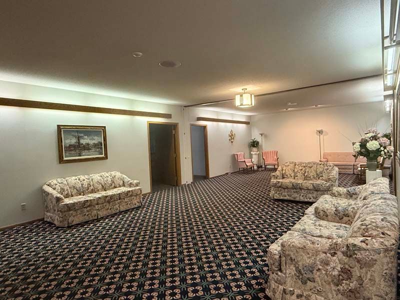 A waiting room with floral sofas, dark patterned carpet, and white walls.