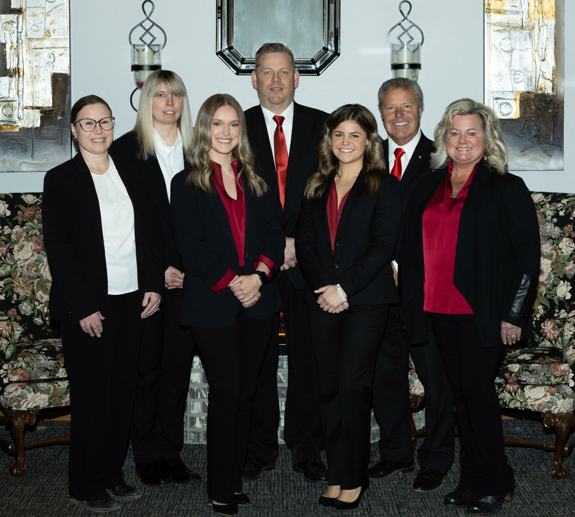 Three people standing in front of a fireplace; two women and a man in formal attire, smiles.