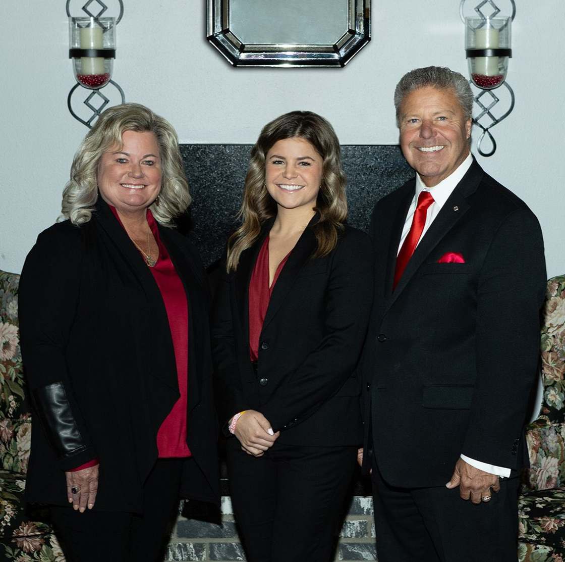 Three people in suits pose in front of a fireplace with decor.