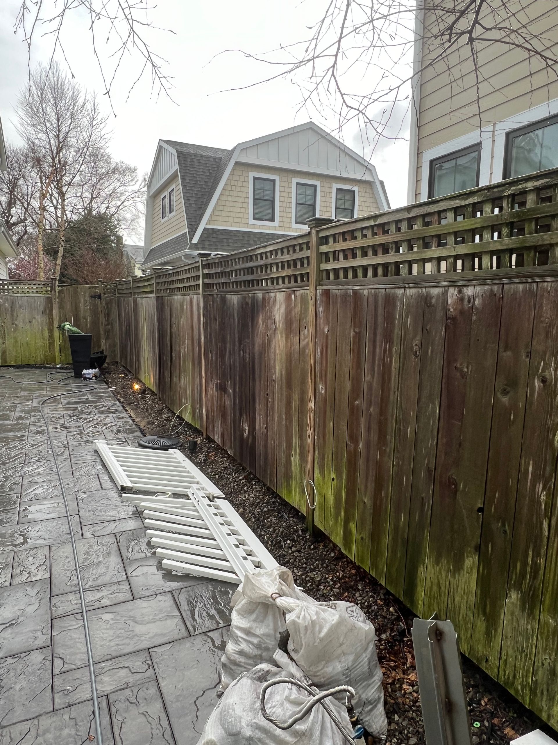 A wooden fence with moss growing on it and a house in the background.