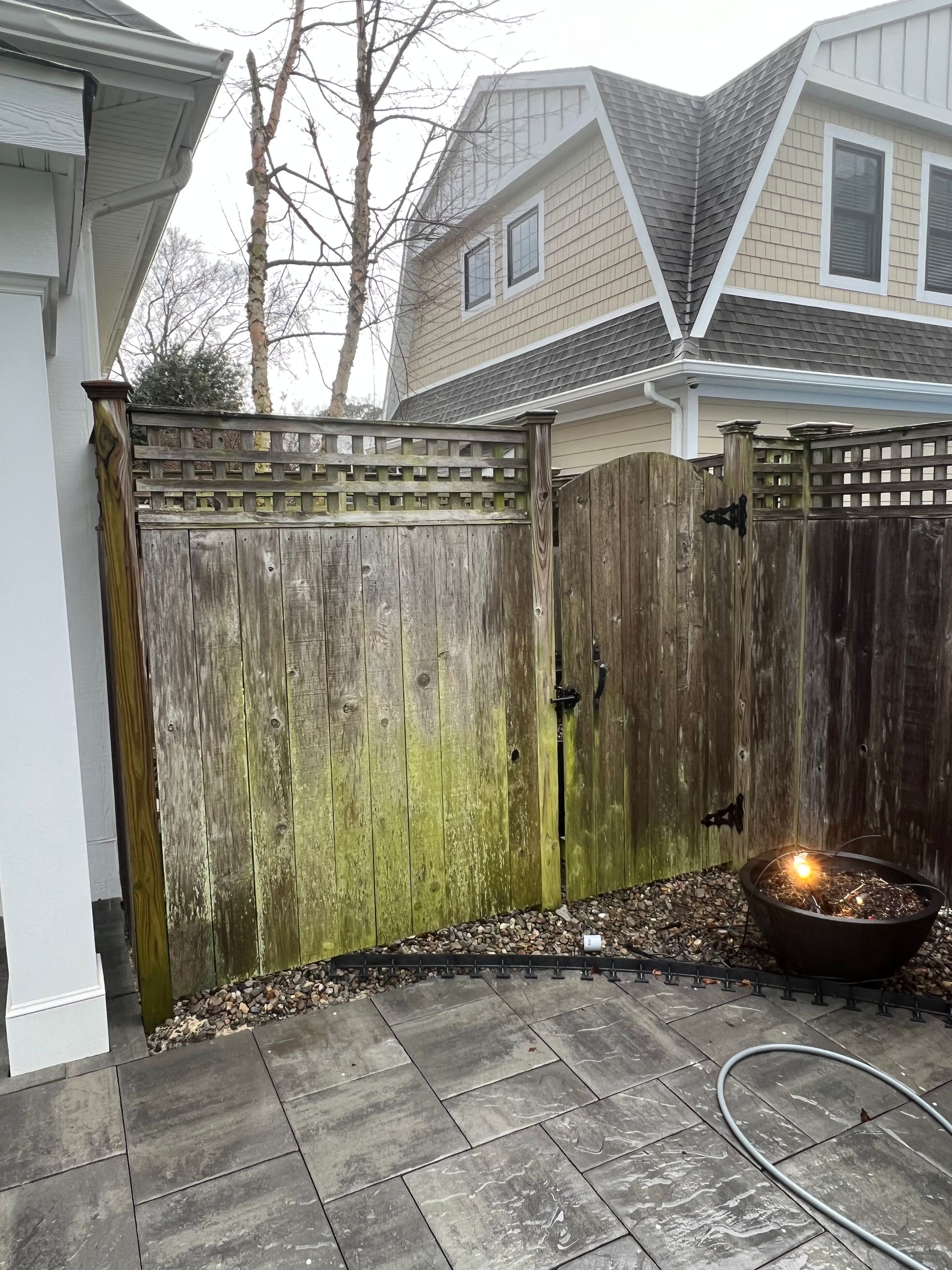 A wooden fence with moss growing on it and a house in the background.