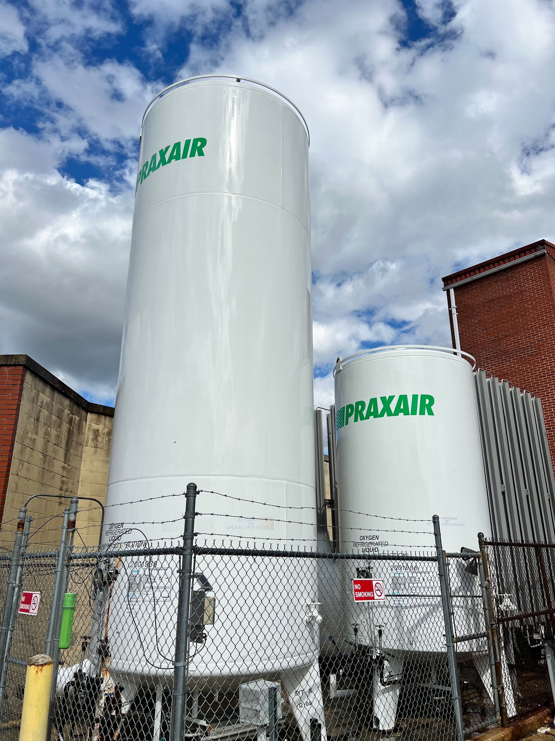 Two large white tanks with the word praxair on them are behind a chain link fence.