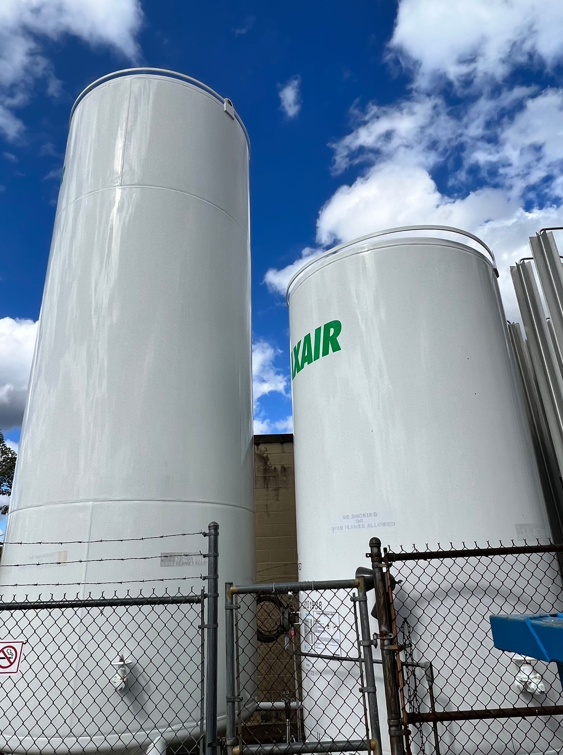 Two large white tanks are behind a chain link fence.