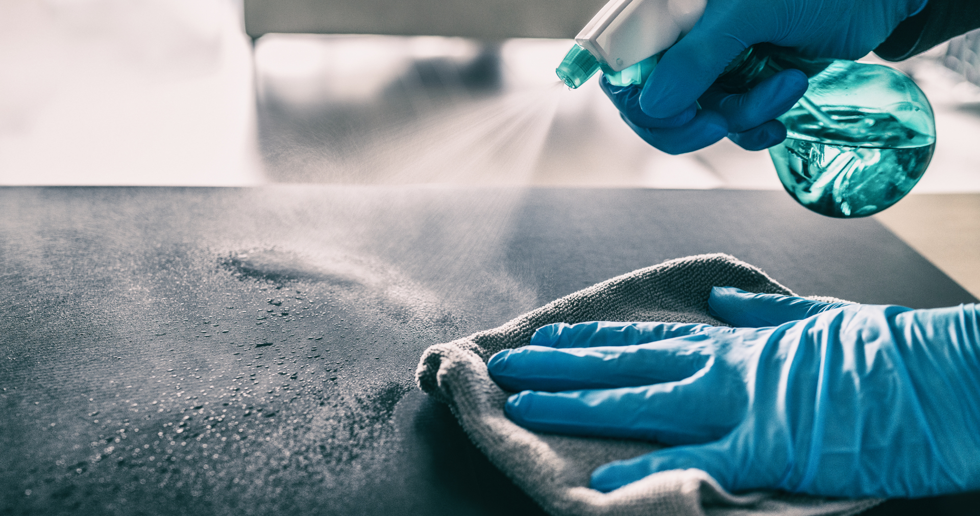 a person wearing blue gloves is cleaning a table with a cloth and spray bottle .