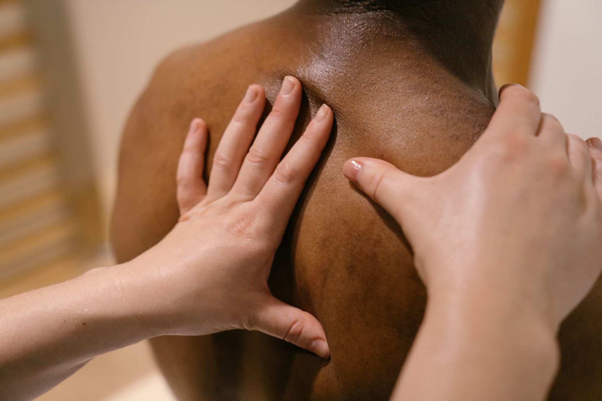 Two hands massage a person's upper back and shoulder during a therapy session