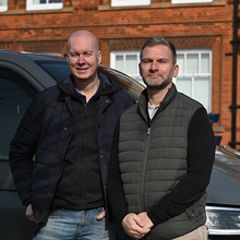 Two men standing next to each other in front of a car