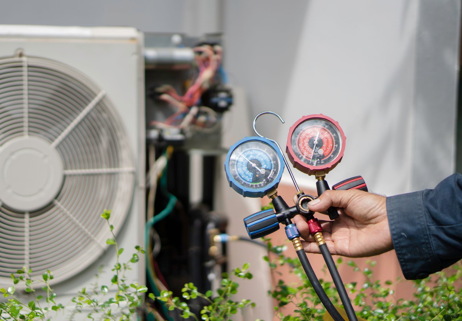HVAC technician holding gauges, checking air conditioning unit outside.