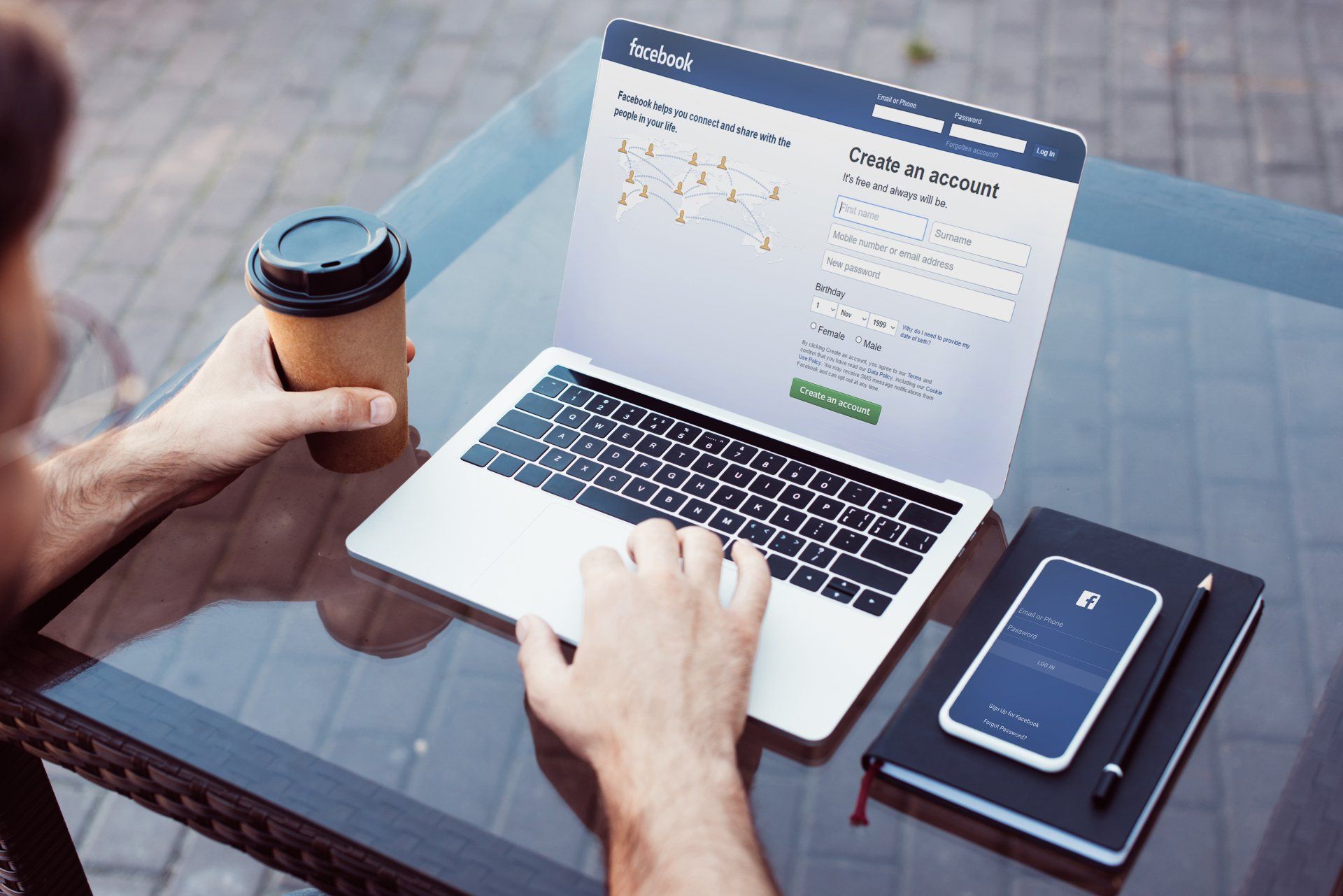 A man is typing on a laptop while holding a cup of coffee