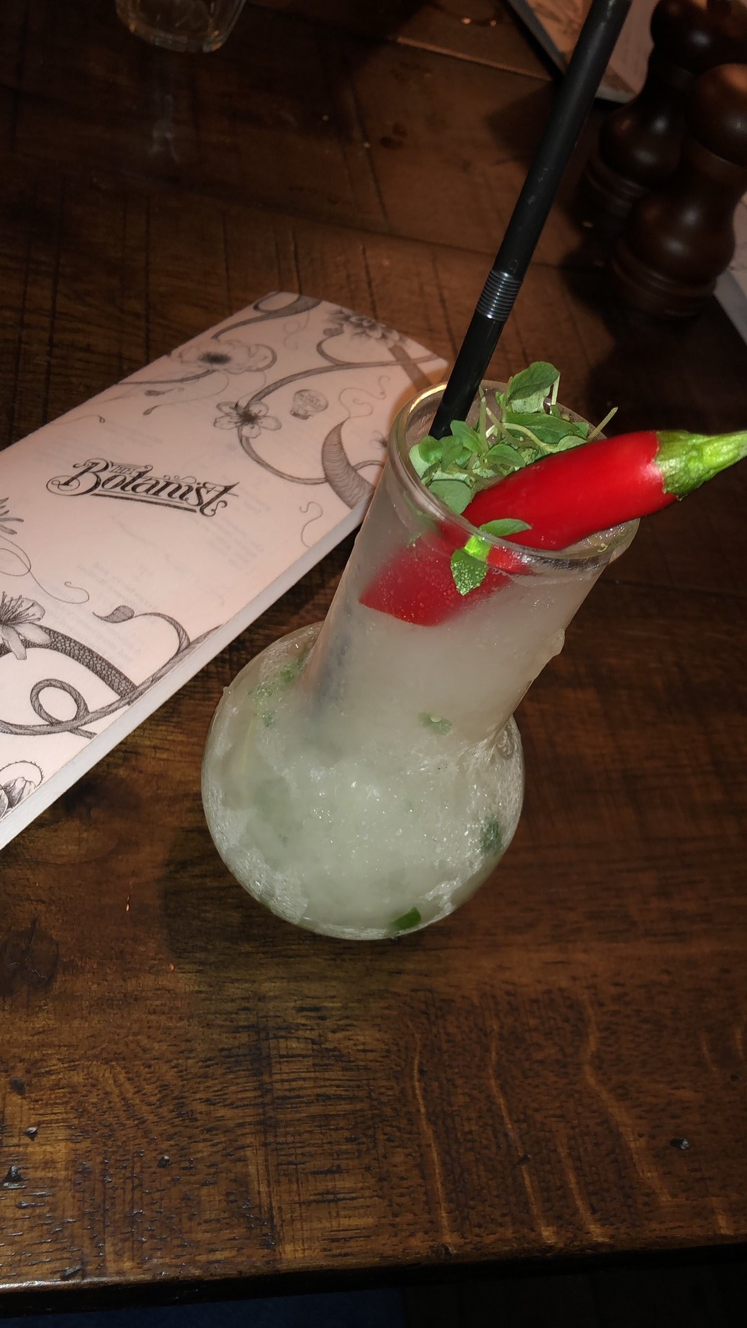 A drink in a glass with a straw and a red pepper on top