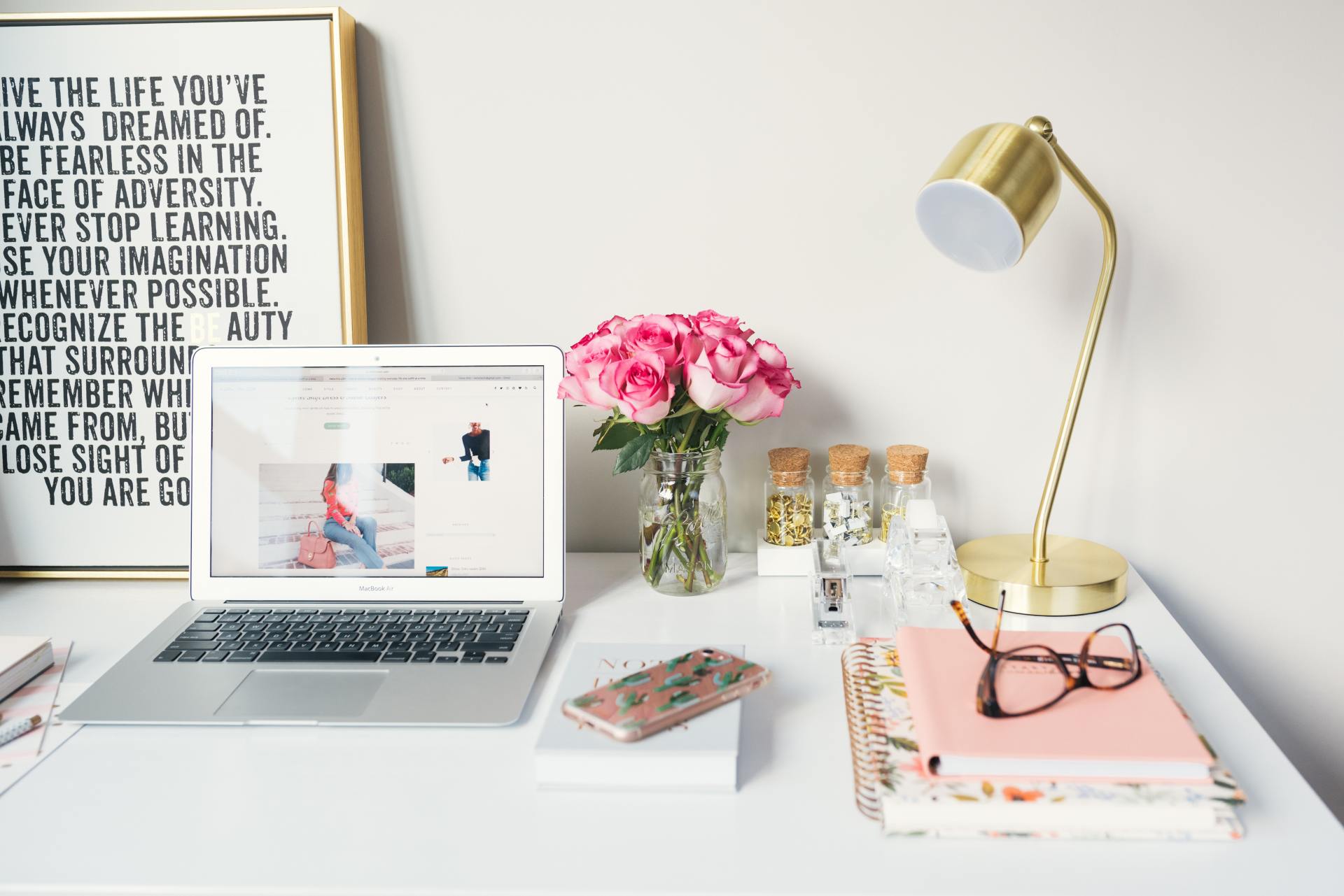 A desk with a laptop and a vase of pink flowers
