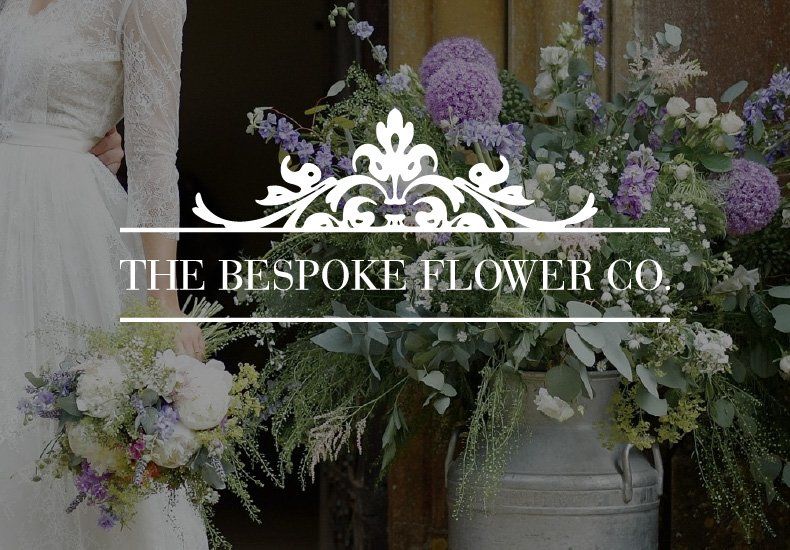A woman in a white dress is holding a bouquet of flowers in front of a sign that says the bespoke flower co.