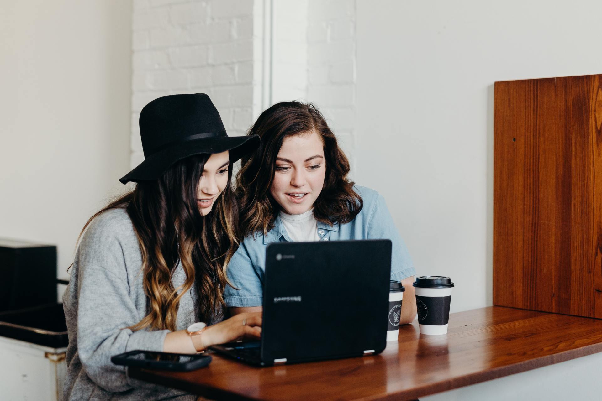 Two women are sitting at a table looking at a laptop.