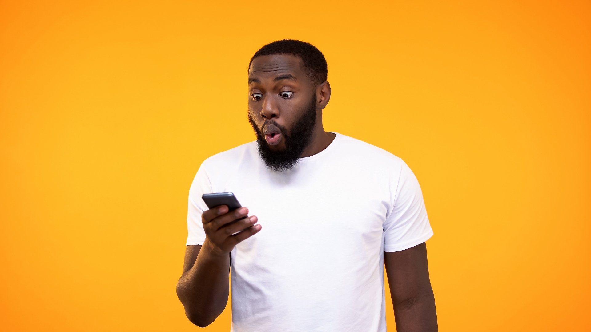 A man with a surprised look on his face is looking at his cell phone.