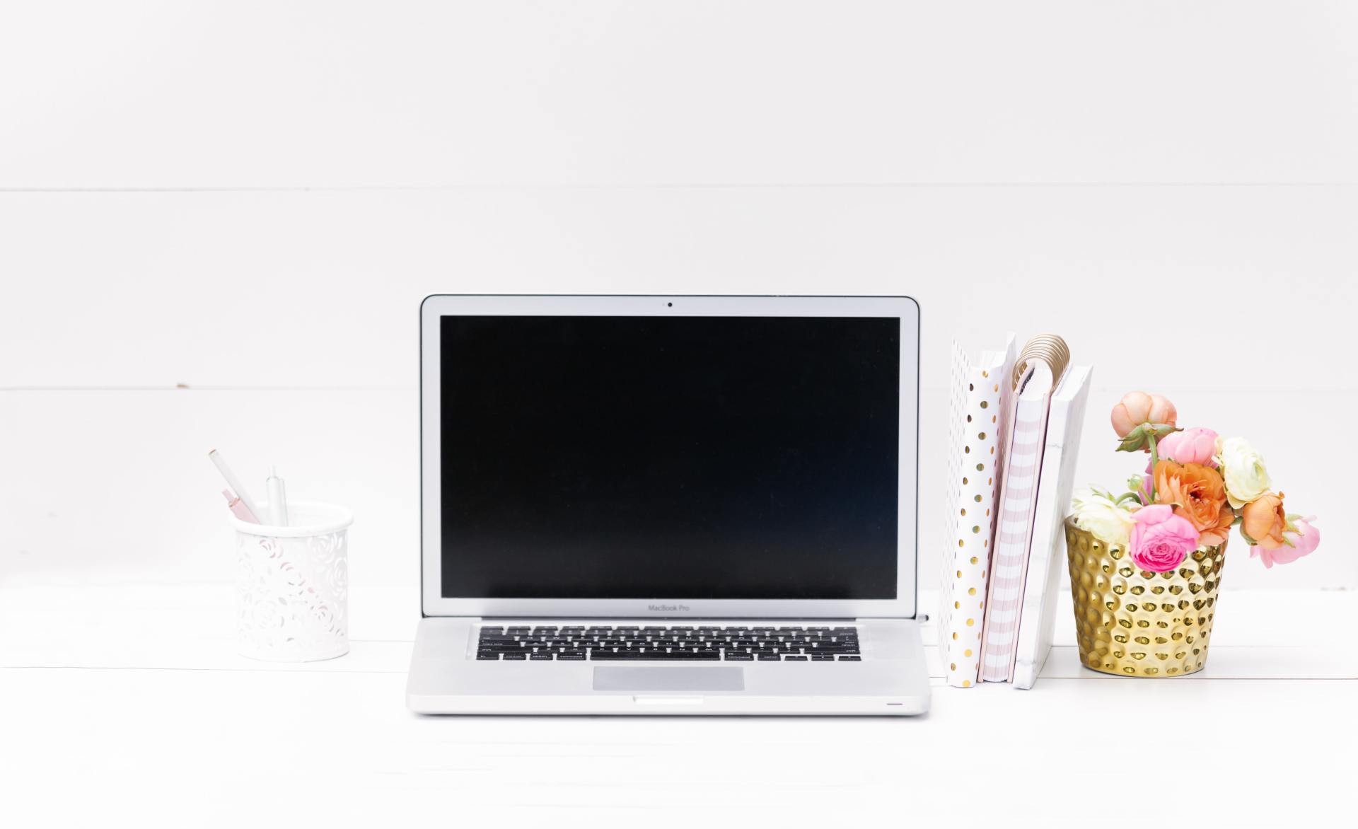 A laptop is open on a desk next to a basket of flowers