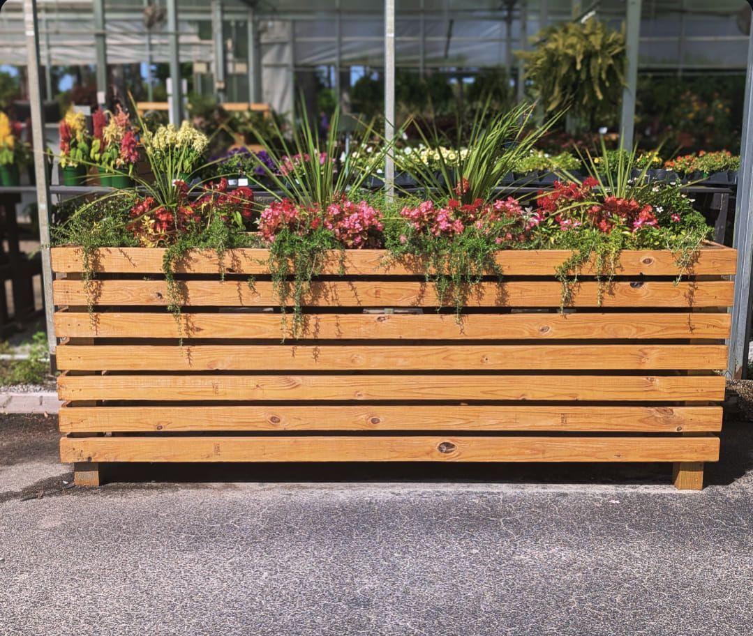 A wooden planter filled with flowers is sitting on the side of the road.