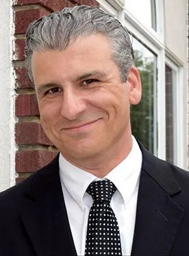 A man in a suit and tie is smiling in front of a brick wall. A man in a suit and tie is smiling in front of a brick wall.