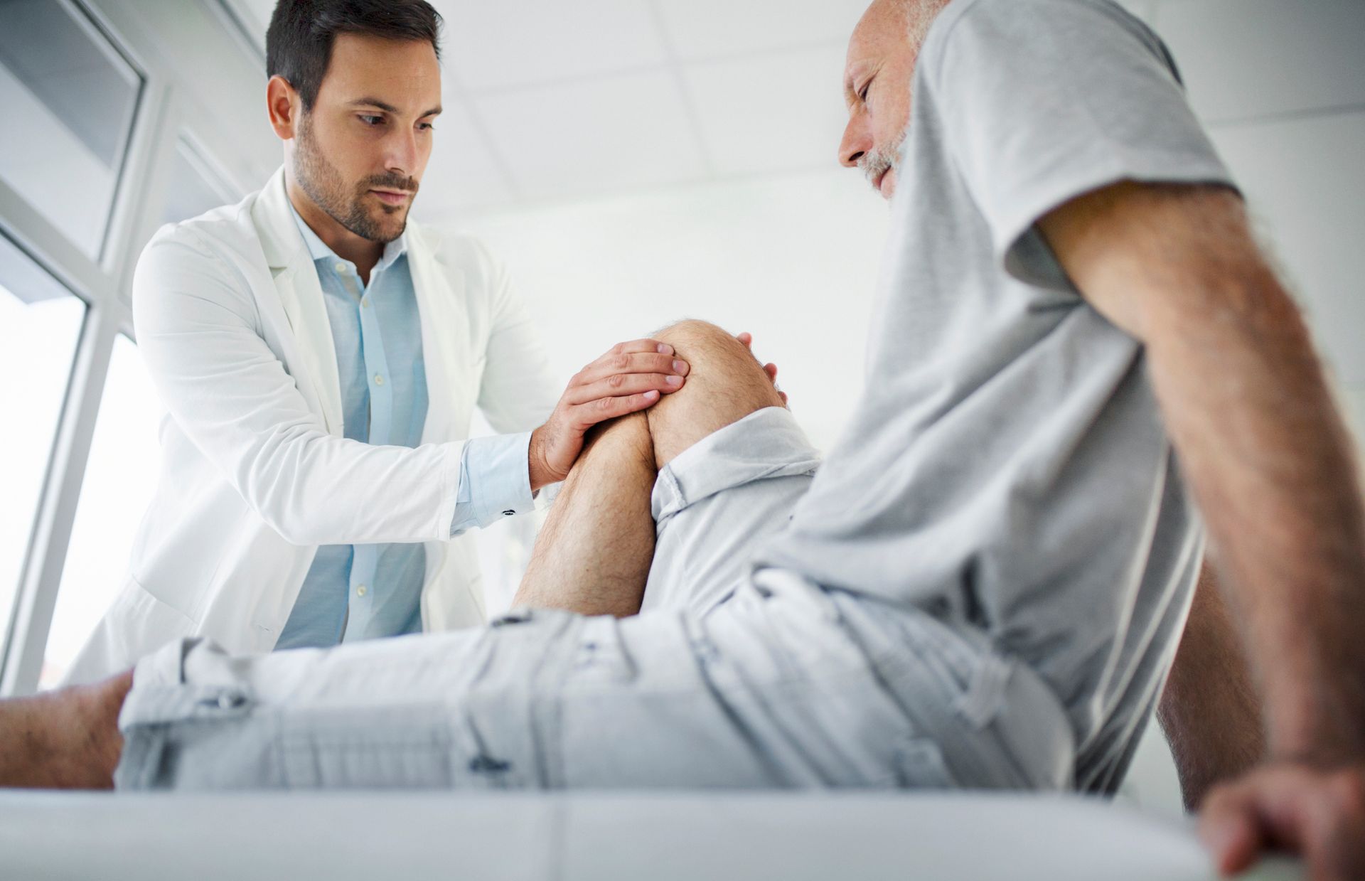 A doctor at a clinic, performing a medical examination on a patient having knee pain. A doctor at a clinic, performing a medical examination on a patient having knee pain.