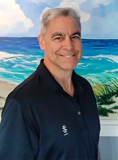 A man in a black shirt is smiling in front of a painting of the ocean. A man in a black shirt is smiling in front of a painting of the ocean.