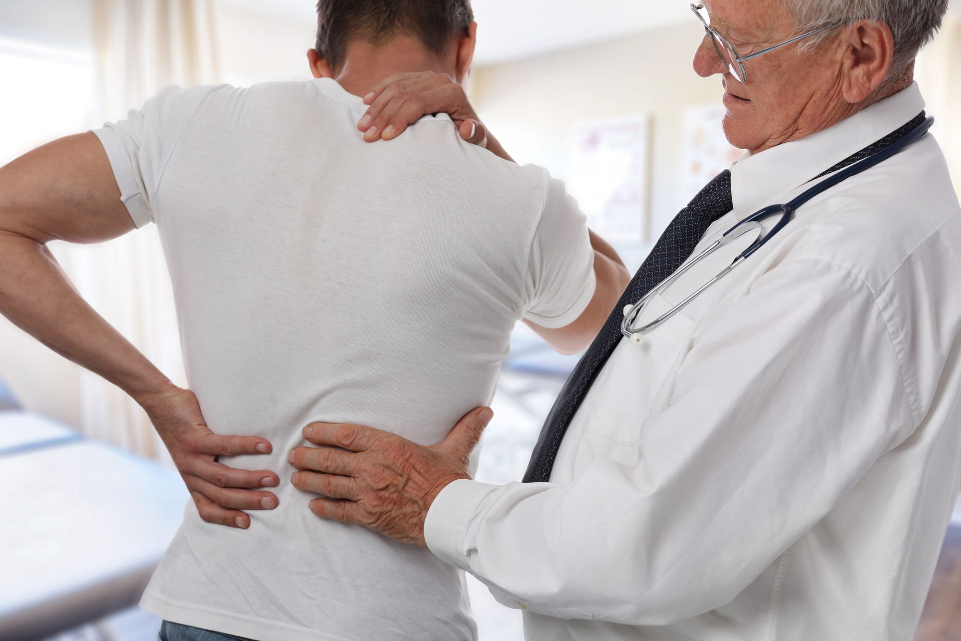 A male chiropractor and patient suffering from back pain during medical exam.