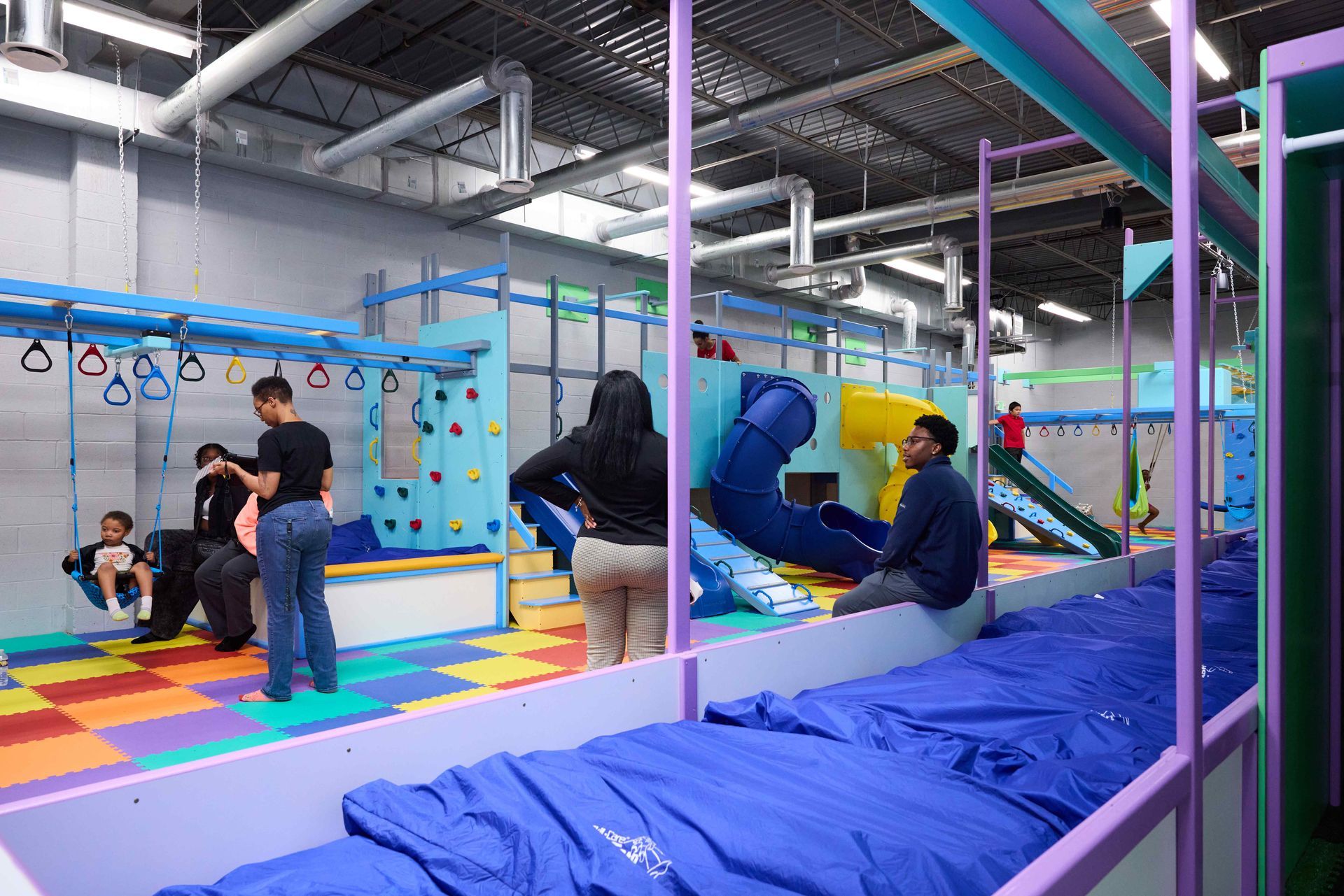 Indoor children’s play area with colorful mats, climbing wall, slides, and kids playing on padded equipment