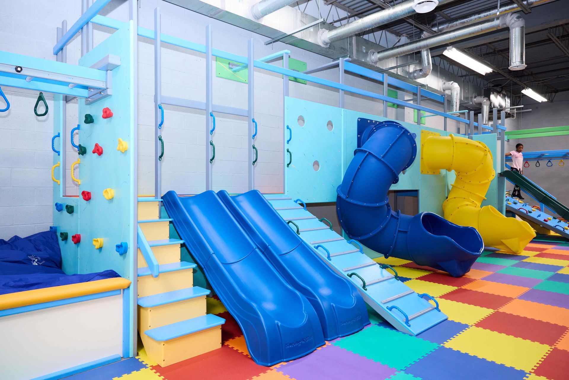 Colorful indoor playroom with blue slides, climbing steps, and padded foam flooring