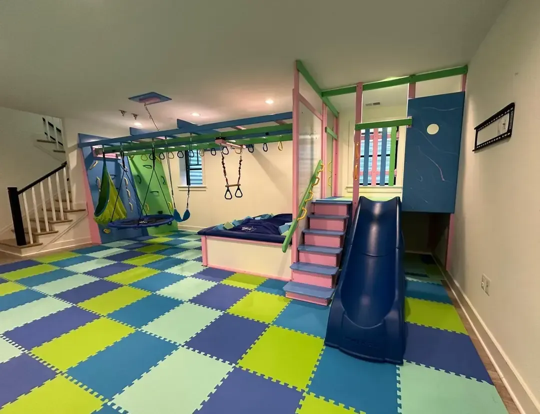 Indoor kids’ playroom with colorful foam floor, climbing structure, slide, and swings