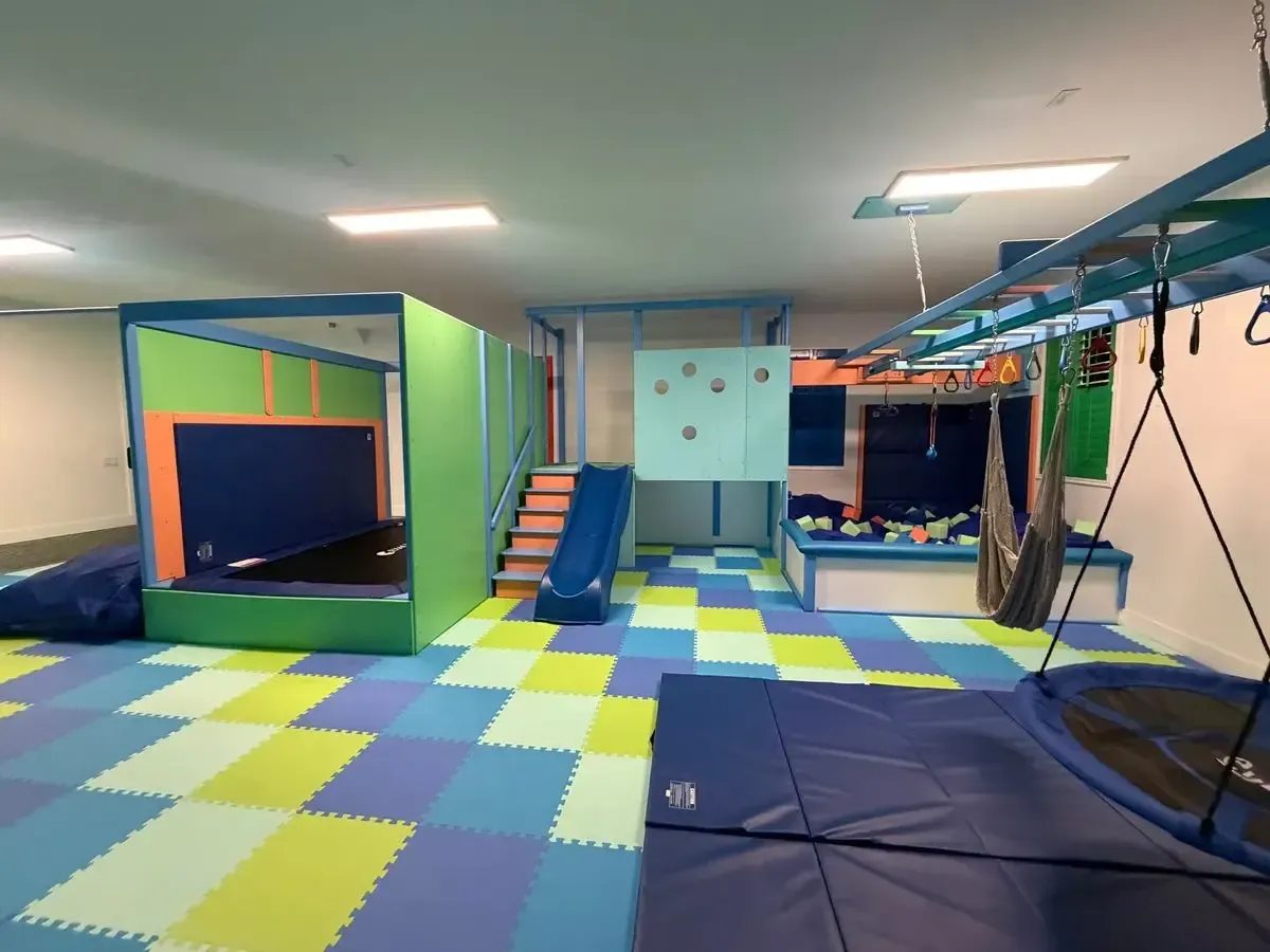 Colorful indoor playroom with foam mats, climbing stairs, nets, and padded equipment