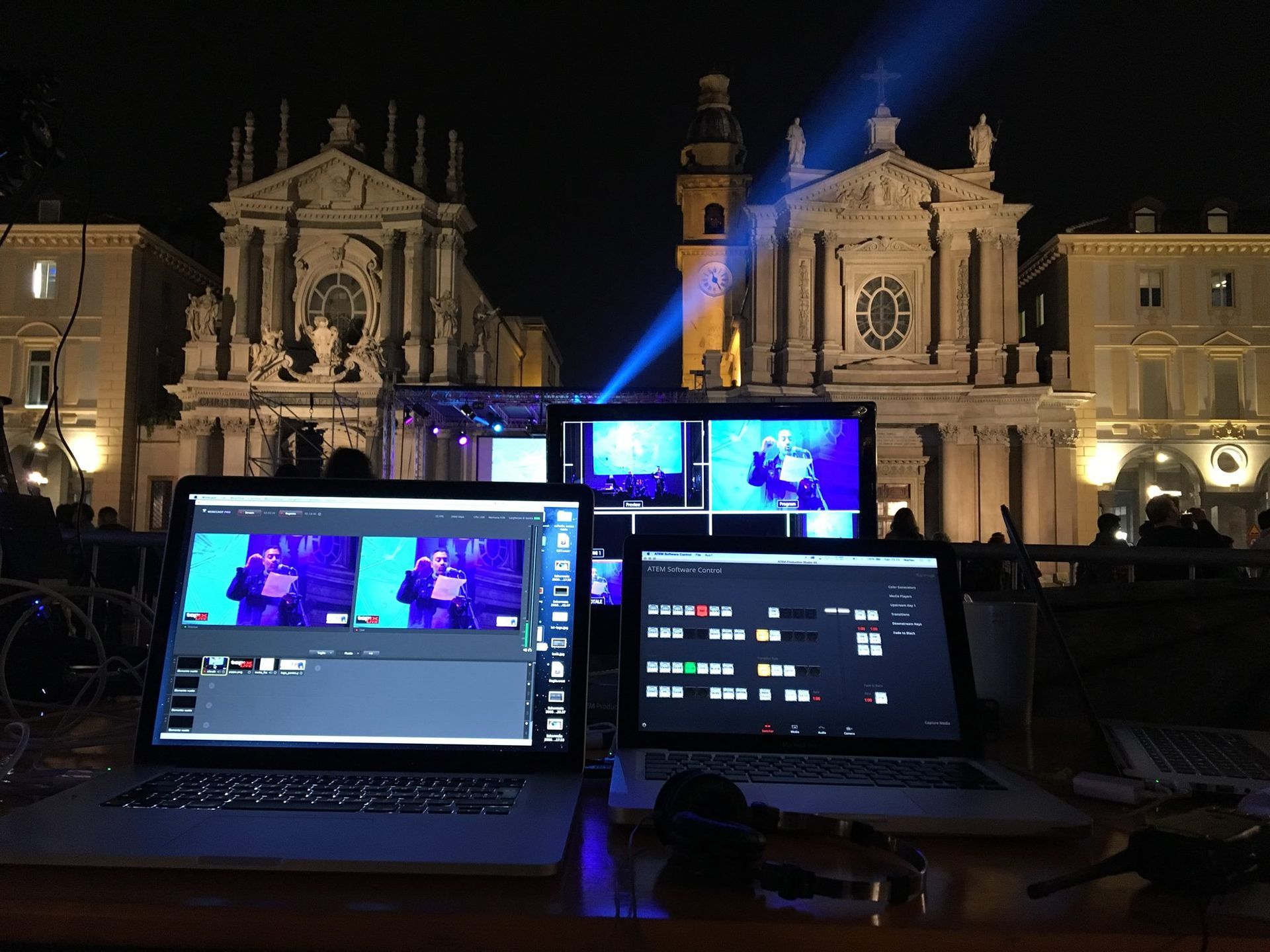 Computer portatili che mostrano riprese in diretta di fronte a un edificio storico di notte, con luci da palcoscenico.