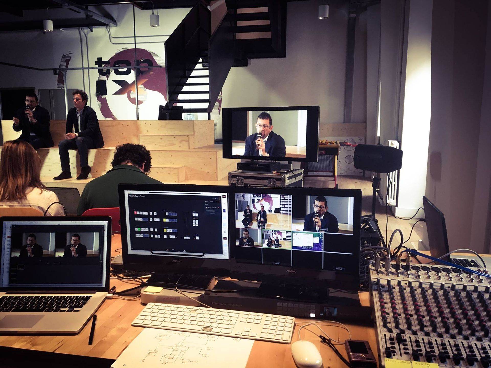 Un evento dal vivo allestito con altoparlanti, monitor e apparecchiature audio in una sede al chiuso.
